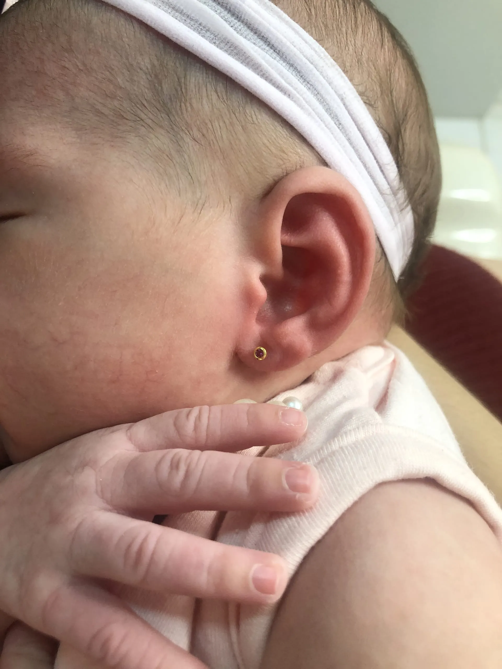 Bebê de faixa branca na cabeça com um brinquinho dourado na orelha